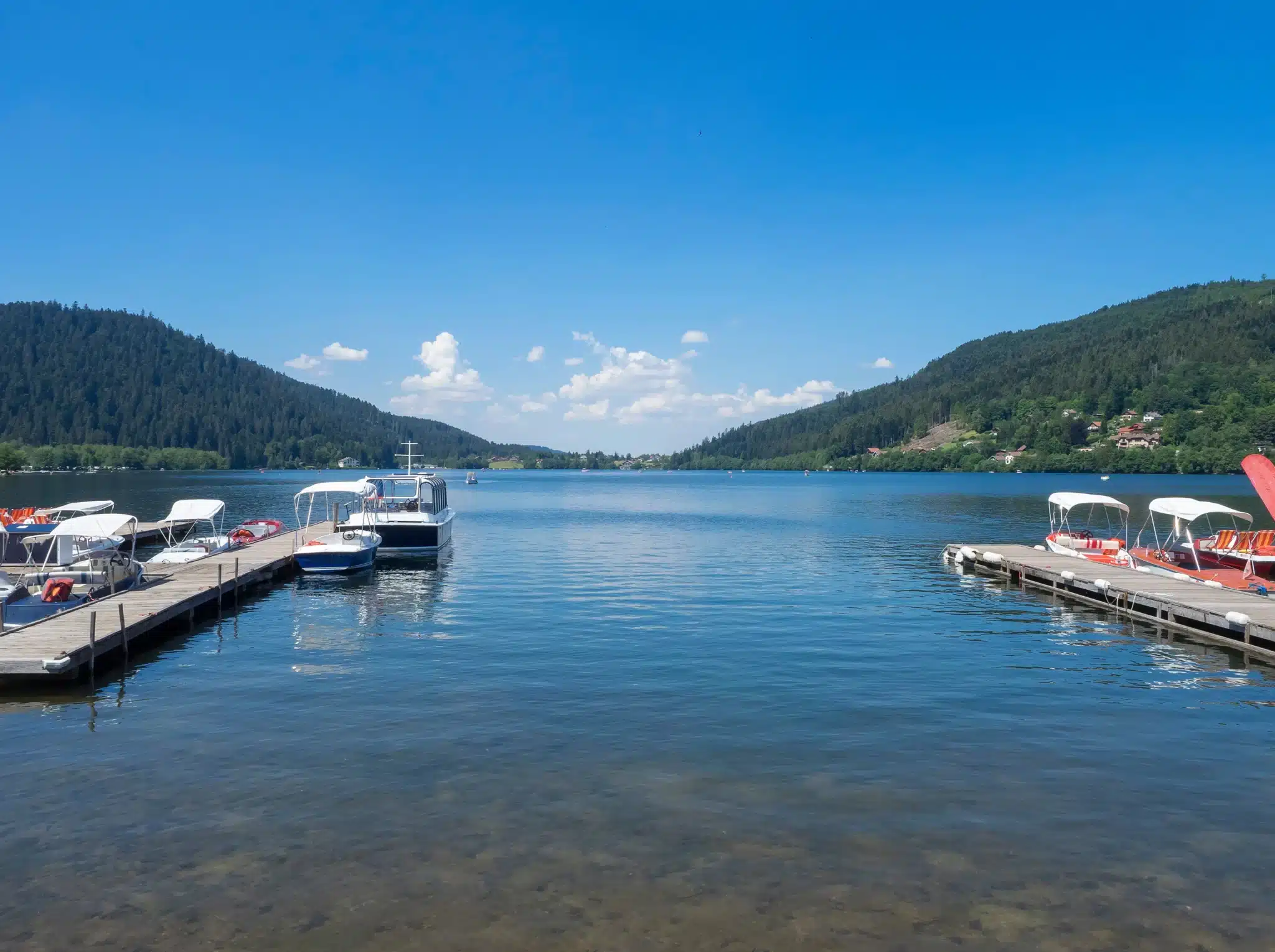 Ponton de bois avec bateaux et campeurs au bord du lac de Gérardmer dans les Vosges.